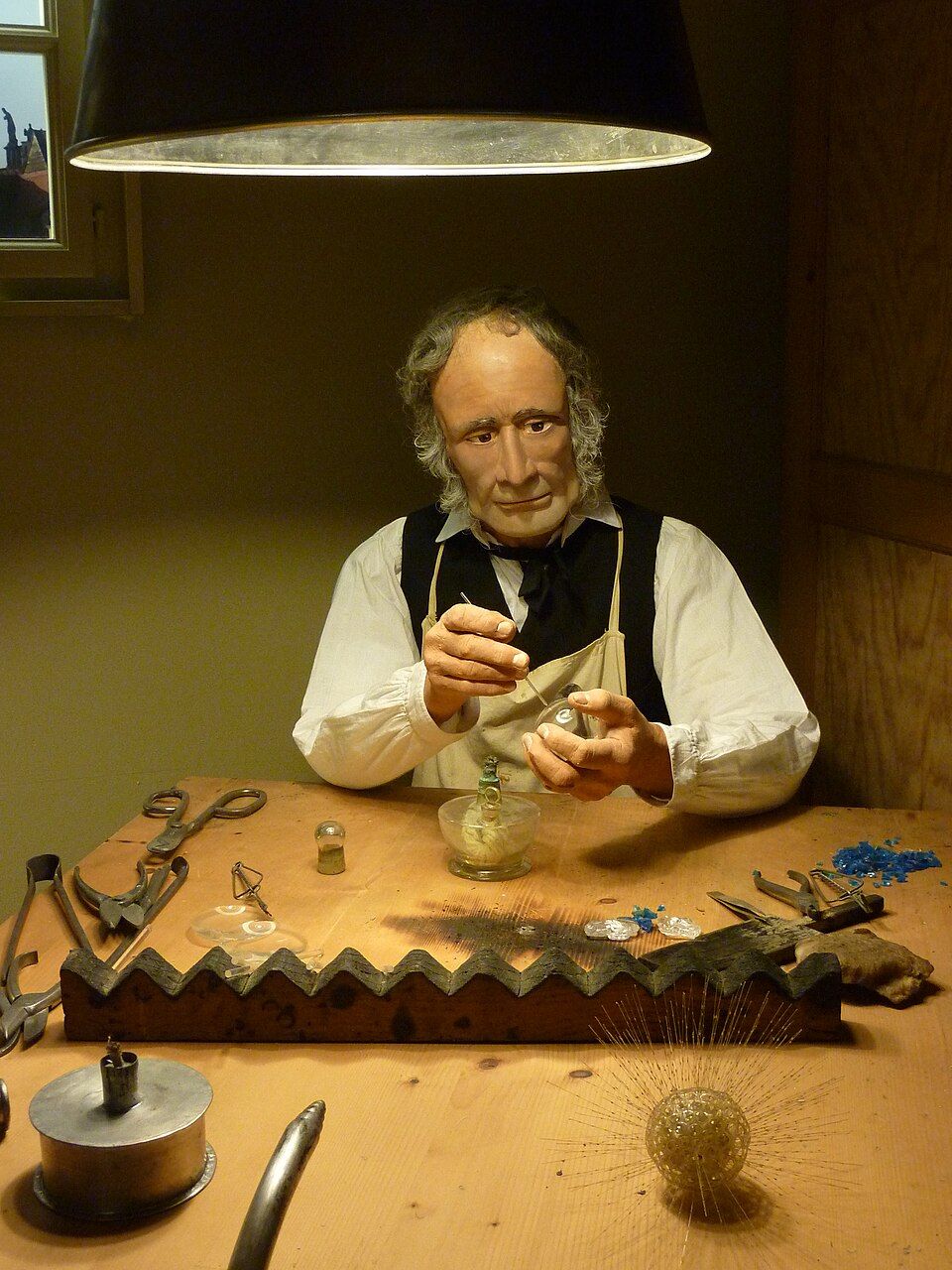 A museum mannequin at a wooden glassworking bench with a bellows beneath it.