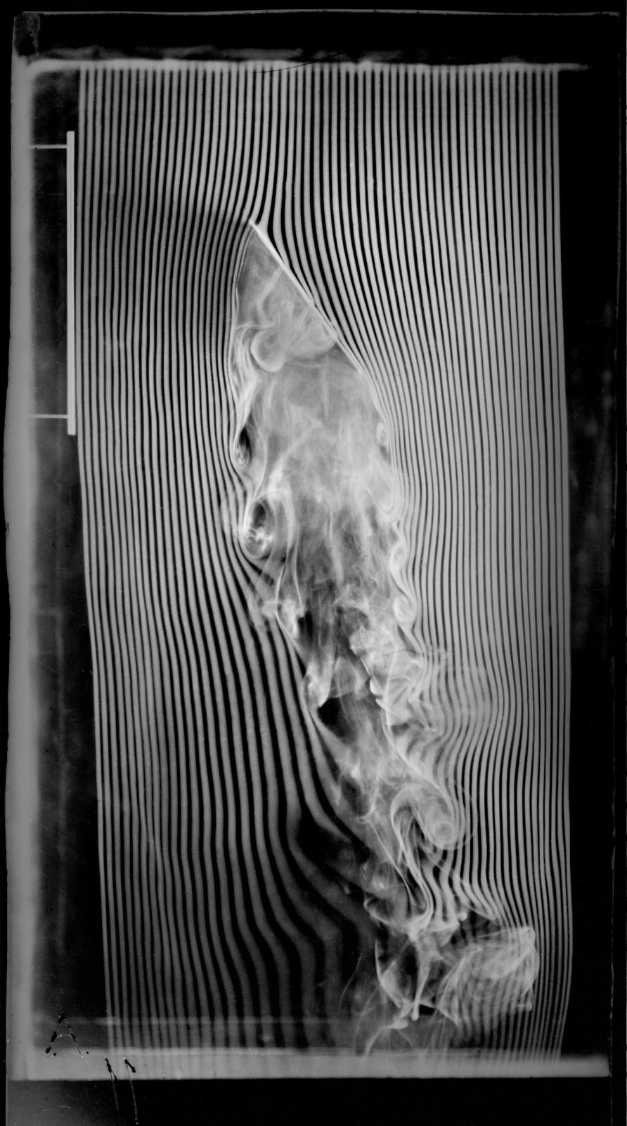 Bright threads of smoke bend around an inclined plate and break into curls in its wake, against a black background.