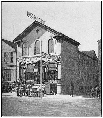 The two-storey Kleinsteuber machine shop, with steps to the entrance and a machine-shop sign above the roof