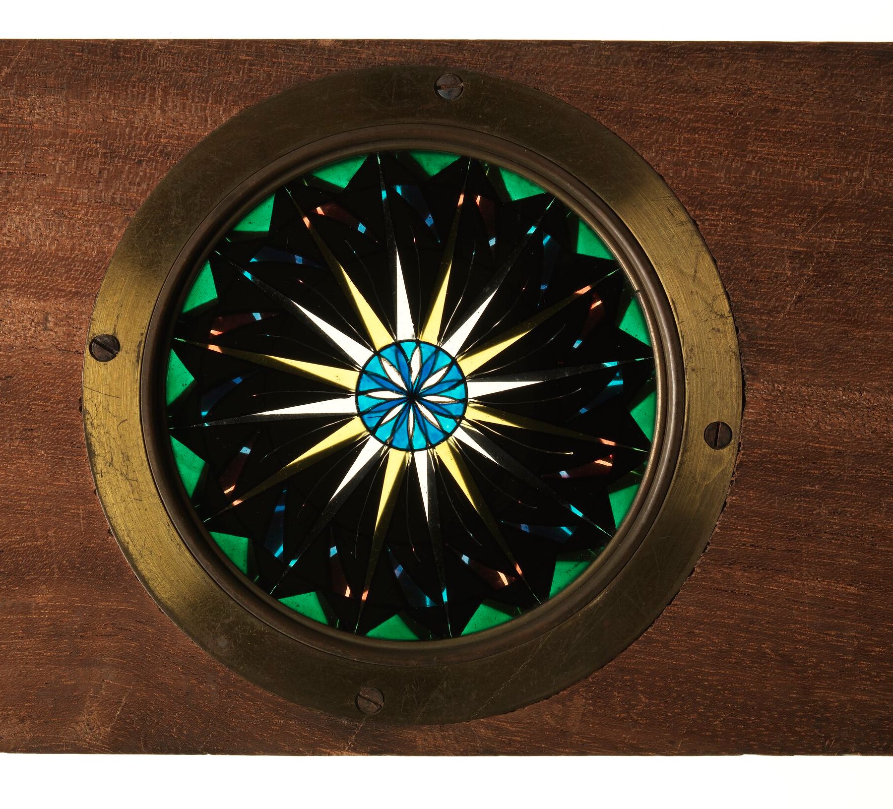 A circular blue, yellow and green pattern sits inside a brass ring in a wooden slide frame.