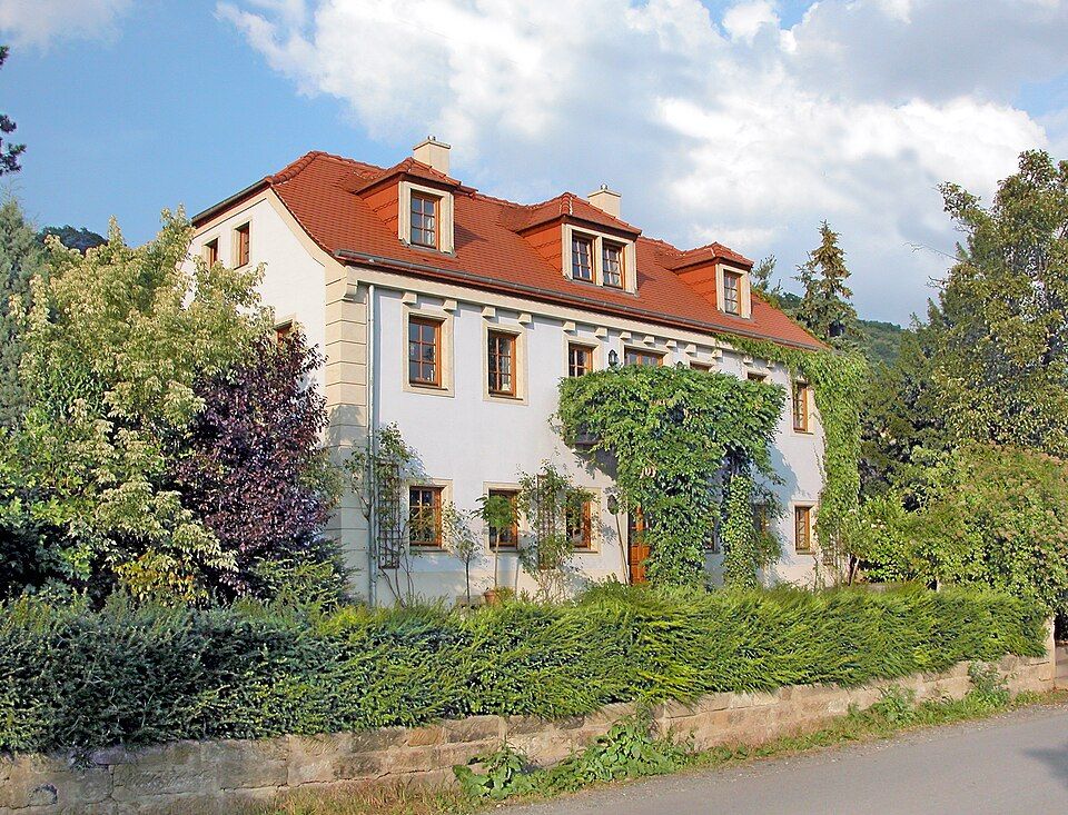 A pale house with a red tiled roof and leafy garden in Hosterwitz.