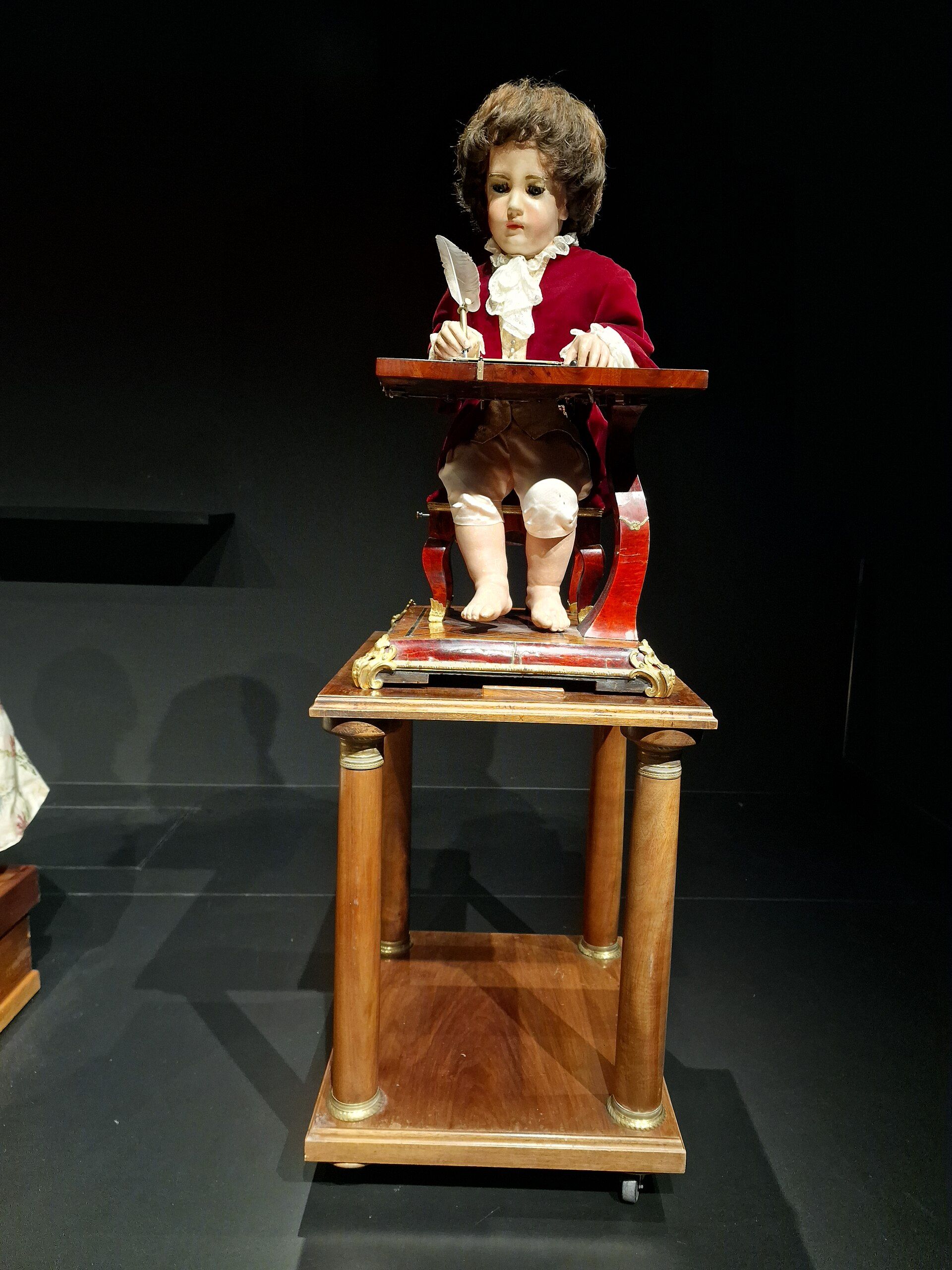 The Writer, a small seated figure in a red coat, holding a quill above a desk.
