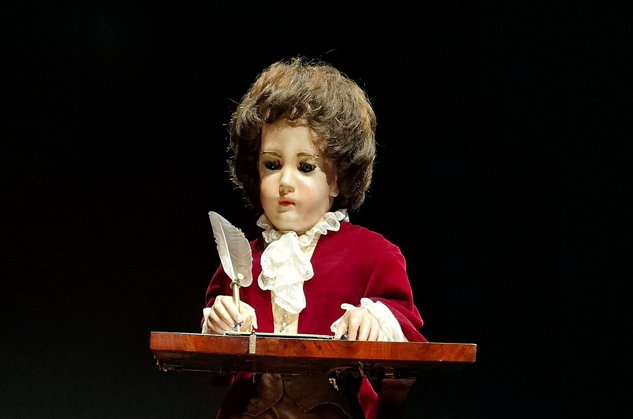 The Writer, a small seated figure in a red coat, holding a quill above a desk.