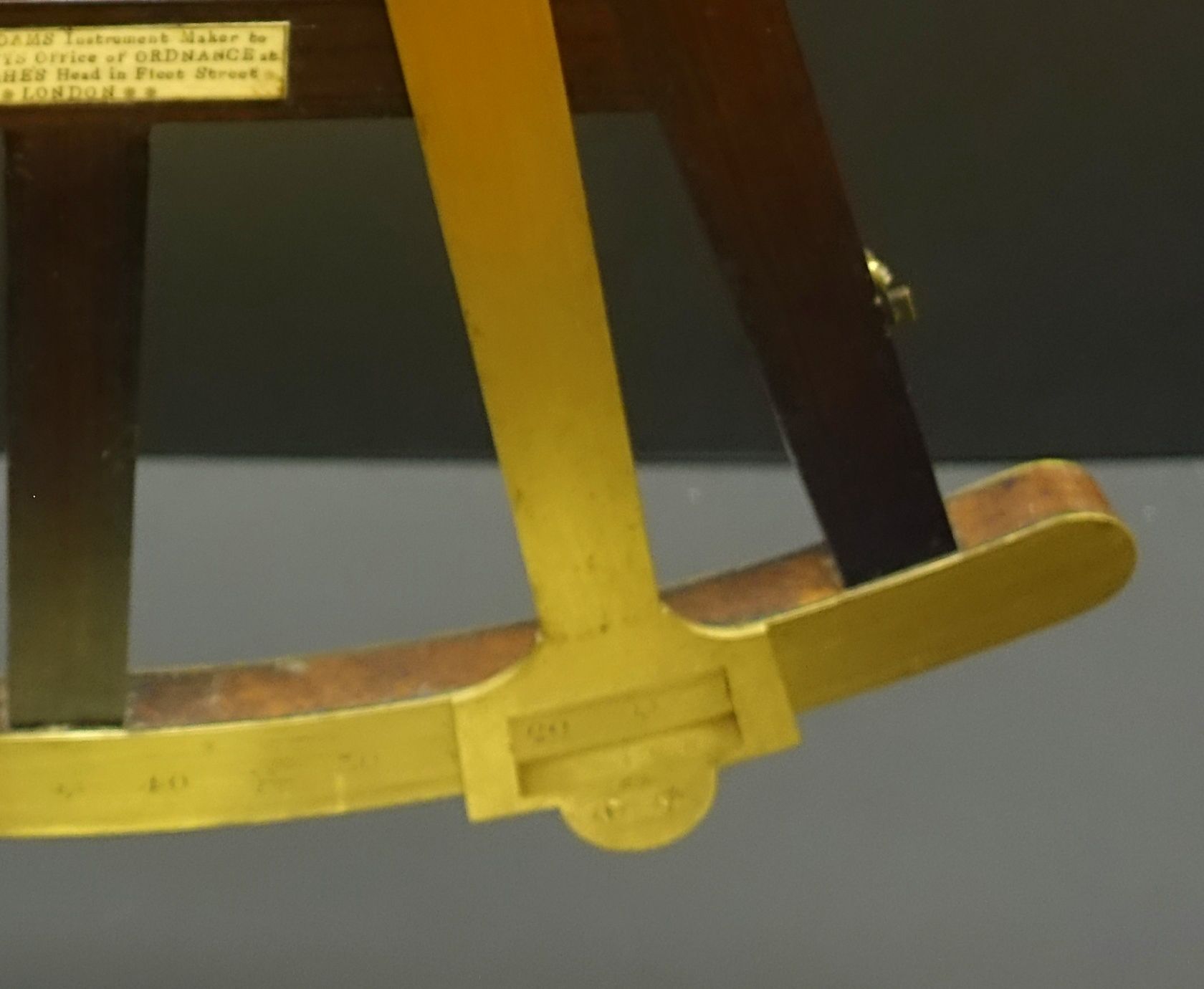 The curved reading scale and brass index arm of a wooden-framed octant