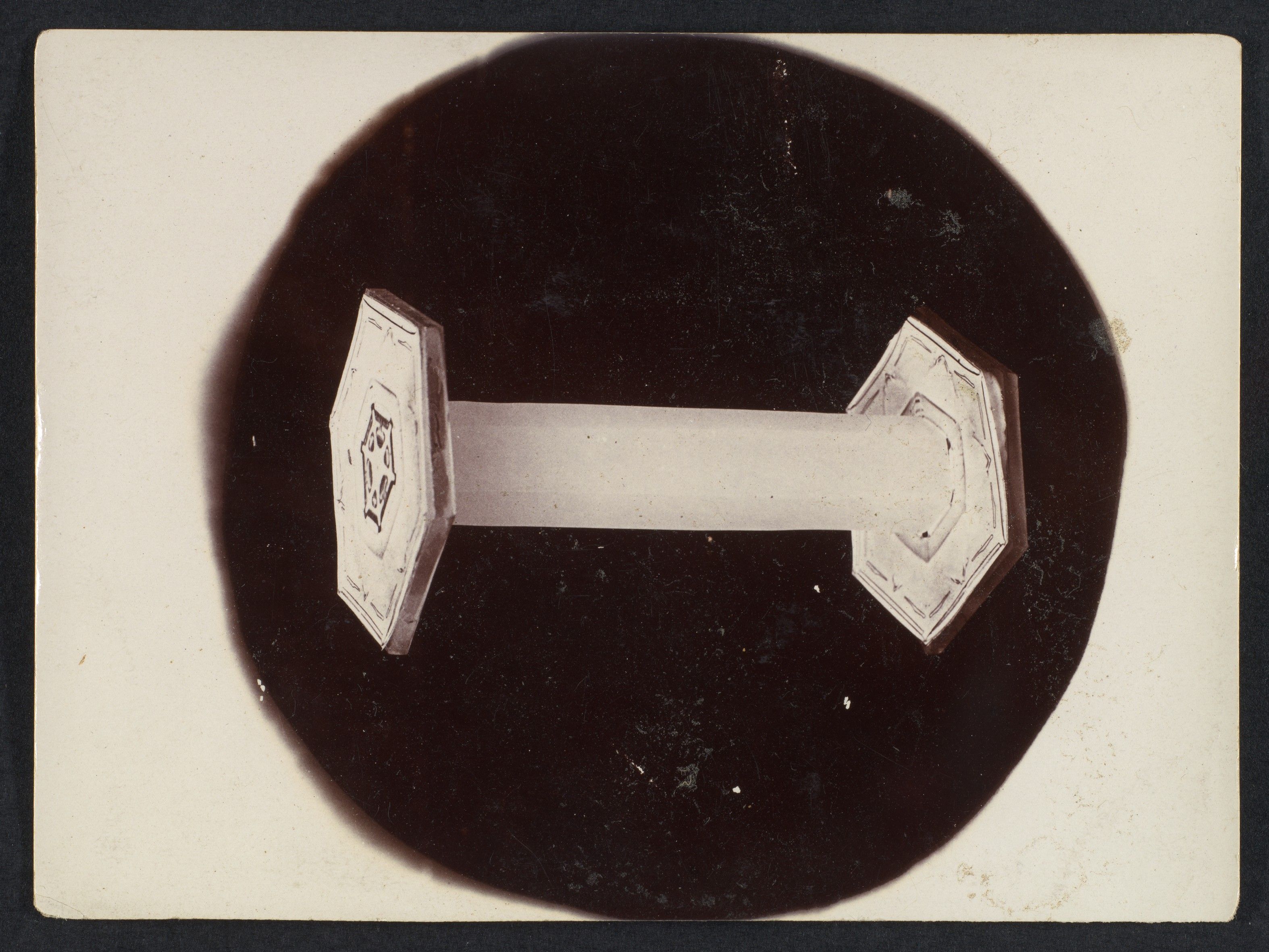 A horizontal column-like snow crystal with plates at its ends, set within a dark circular field.
