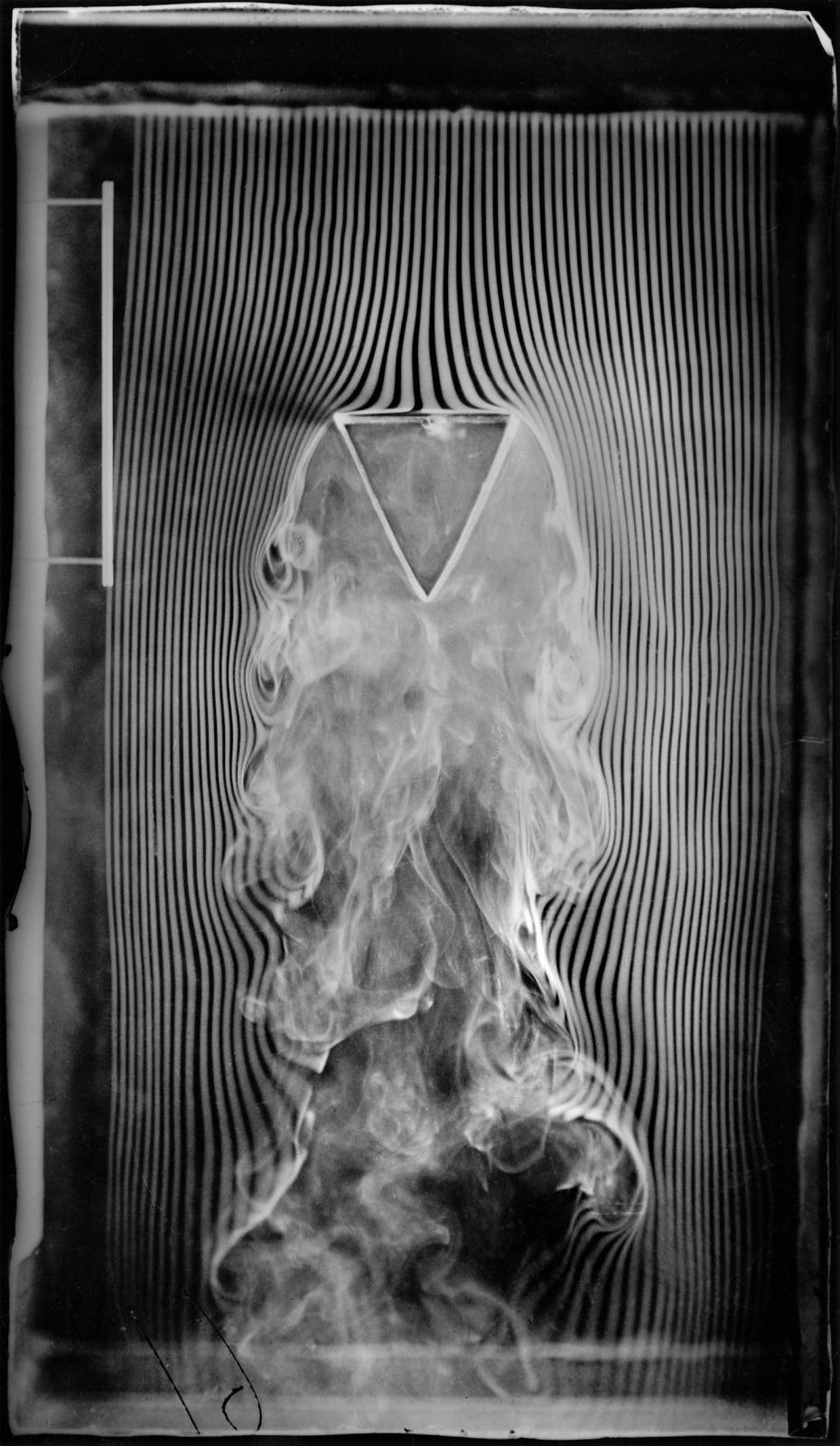 Smoke threads separate around the broad upper face of a triangular prism, leaving an irregular wake below its downward point.