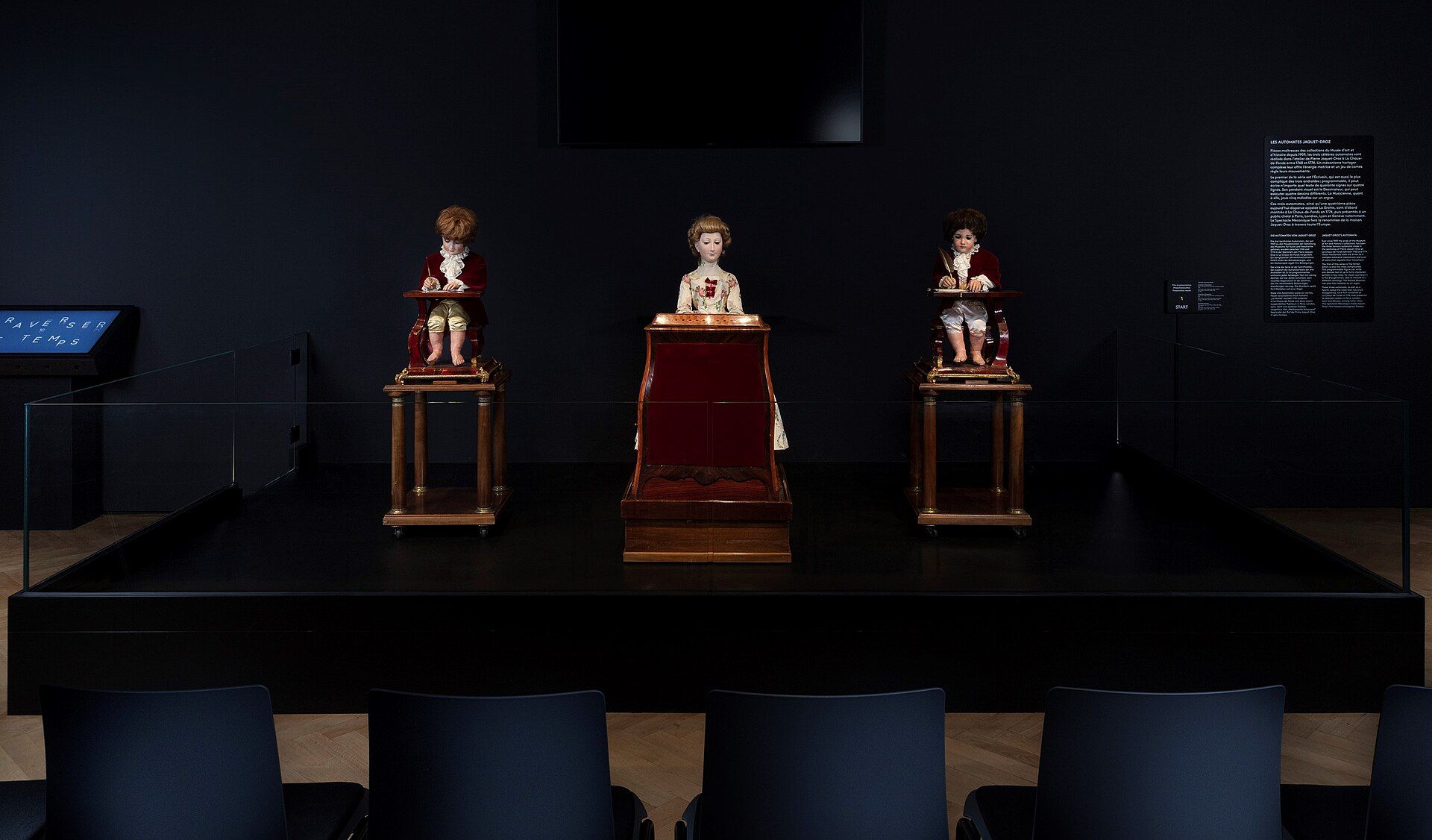The three Jaquet-Droz automata displayed together on a museum stage before rows of seats.
