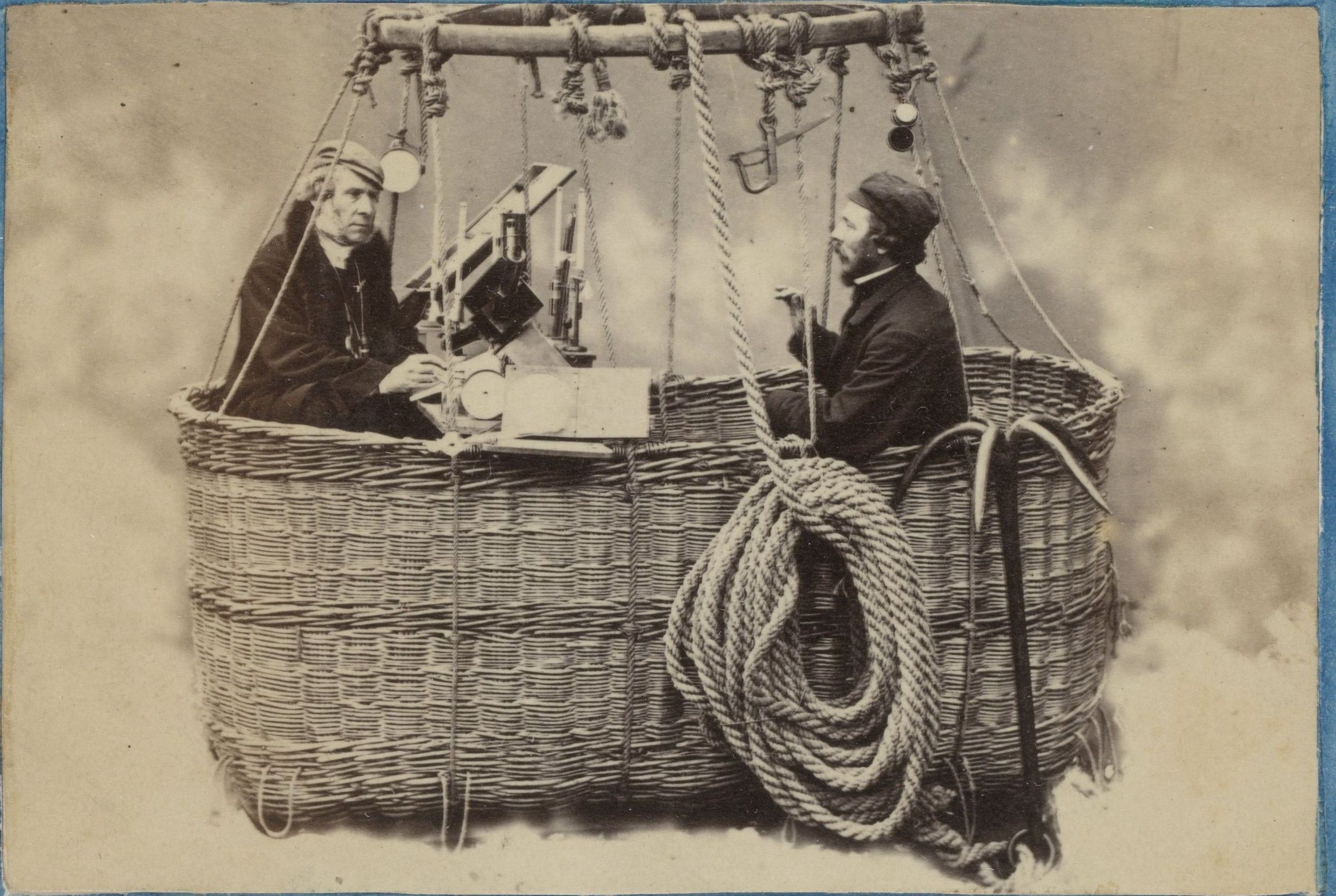 James Glaisher and Henry Coxwell sit on opposite sides of a table of instruments in a wicker balloon basket