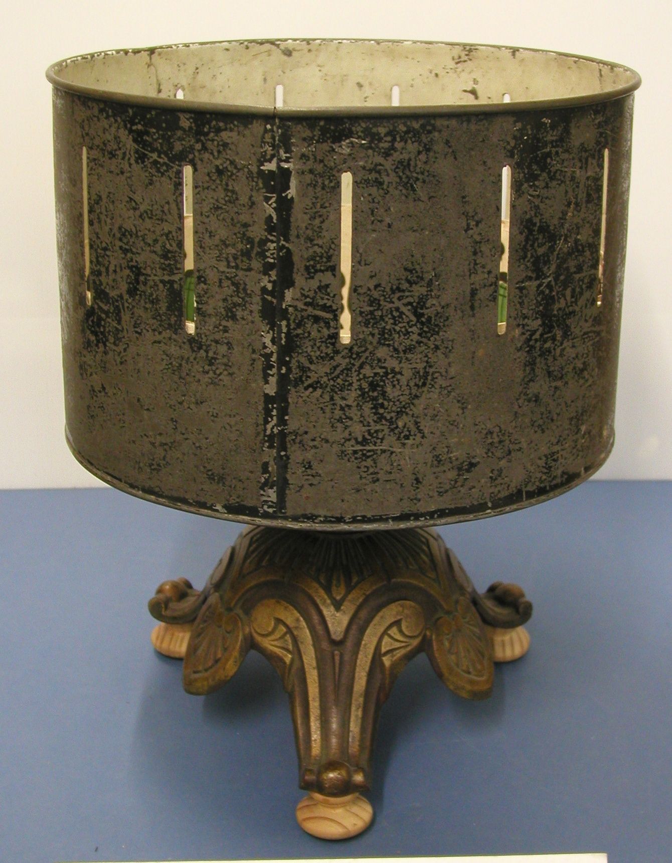 A weathered black zoetrope drum with narrow vertical slots, standing on an ornamental three-footed base