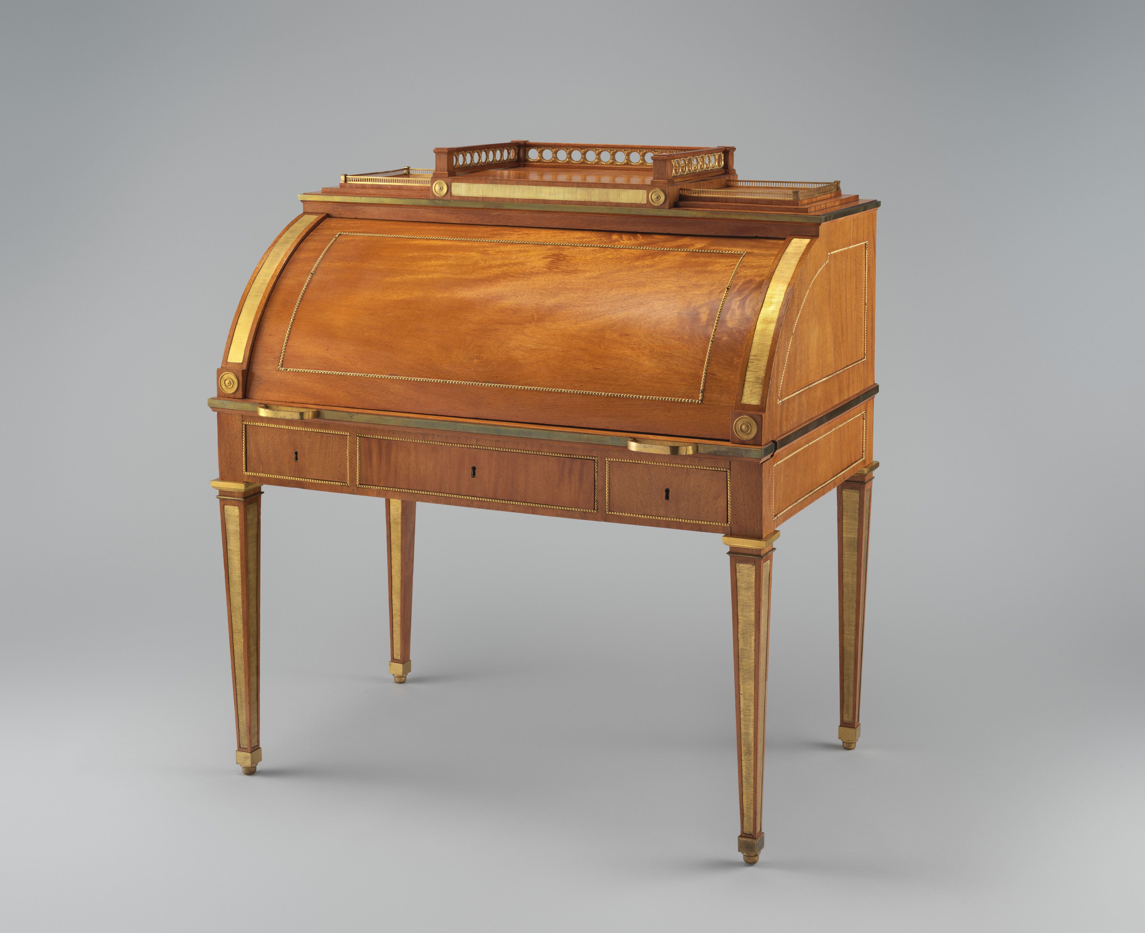 A yellowheart rolltop desk closed, with curved wooden cover, bronze mounts and four tapered legs.