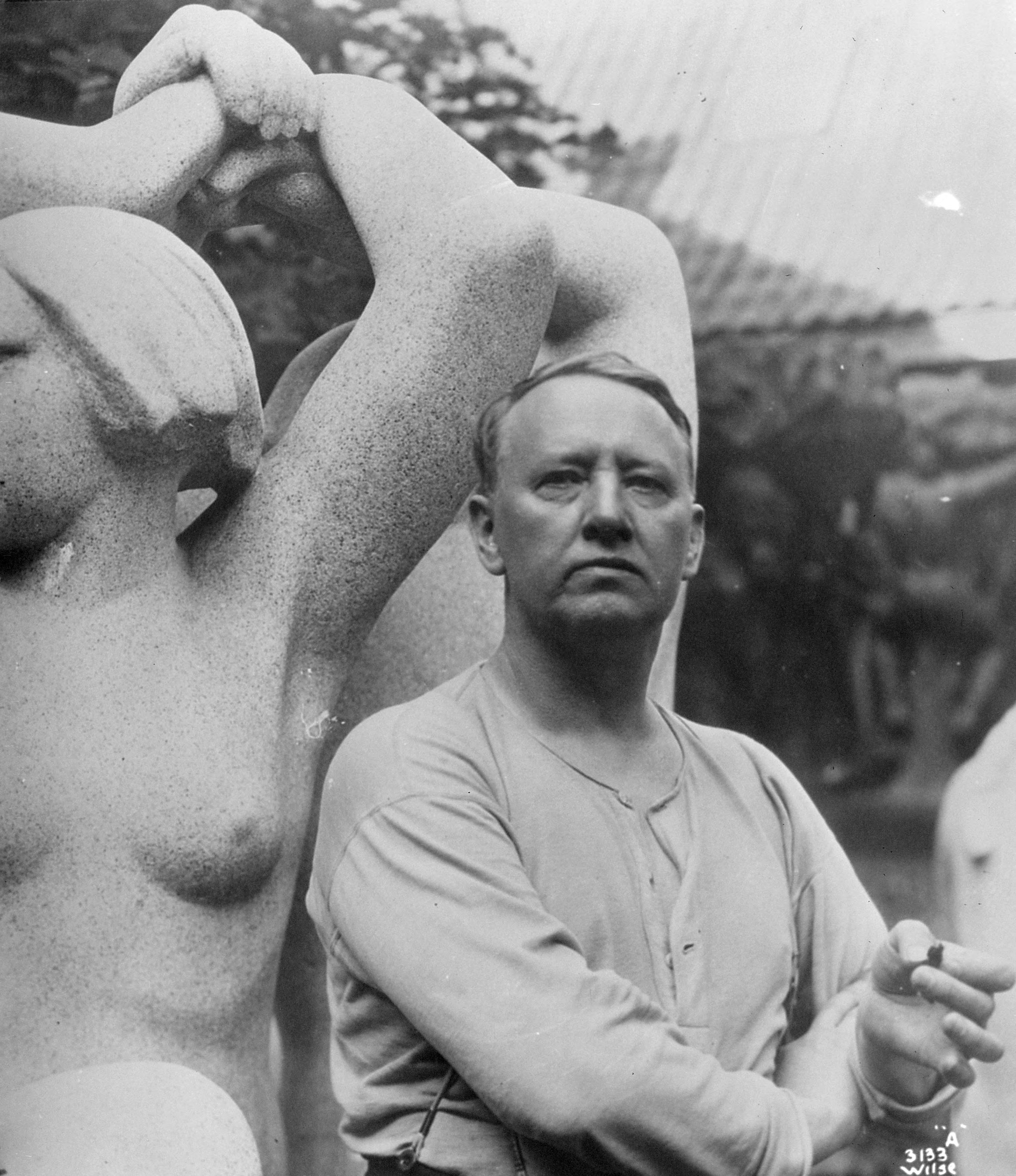 Gustav Vigeland standing beside a granite sculpture, with his hands together.