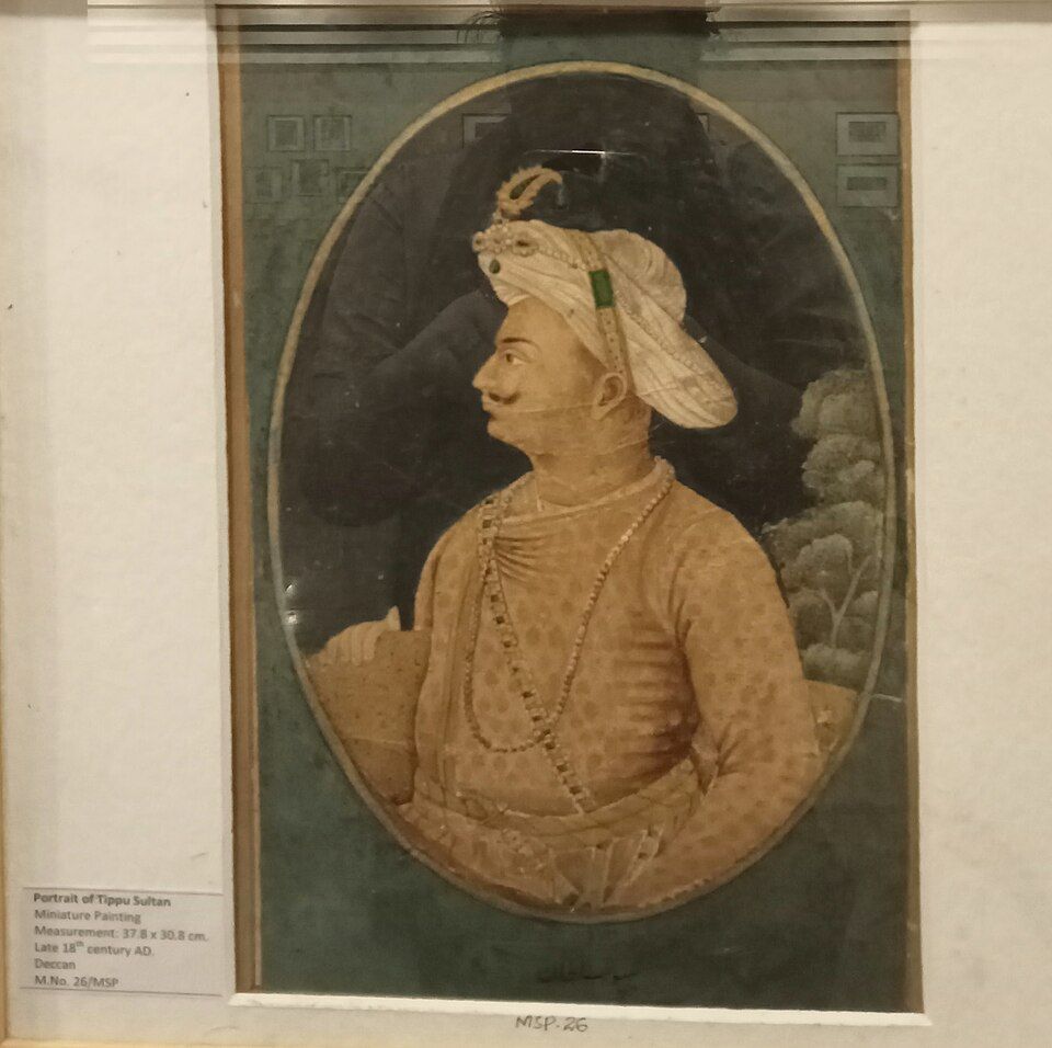 An oval painted portrait of Tipu Sultan wearing a turban and patterned coat.