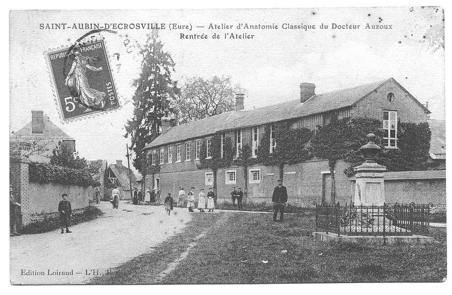 A long two-storey factory building on a village street, with people outside.