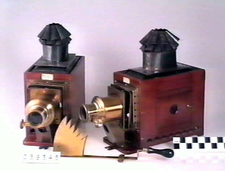 Two mahogany lantern projectors stand beside each other, with brass lens barrels and a fan-shaped metal shutter in front.