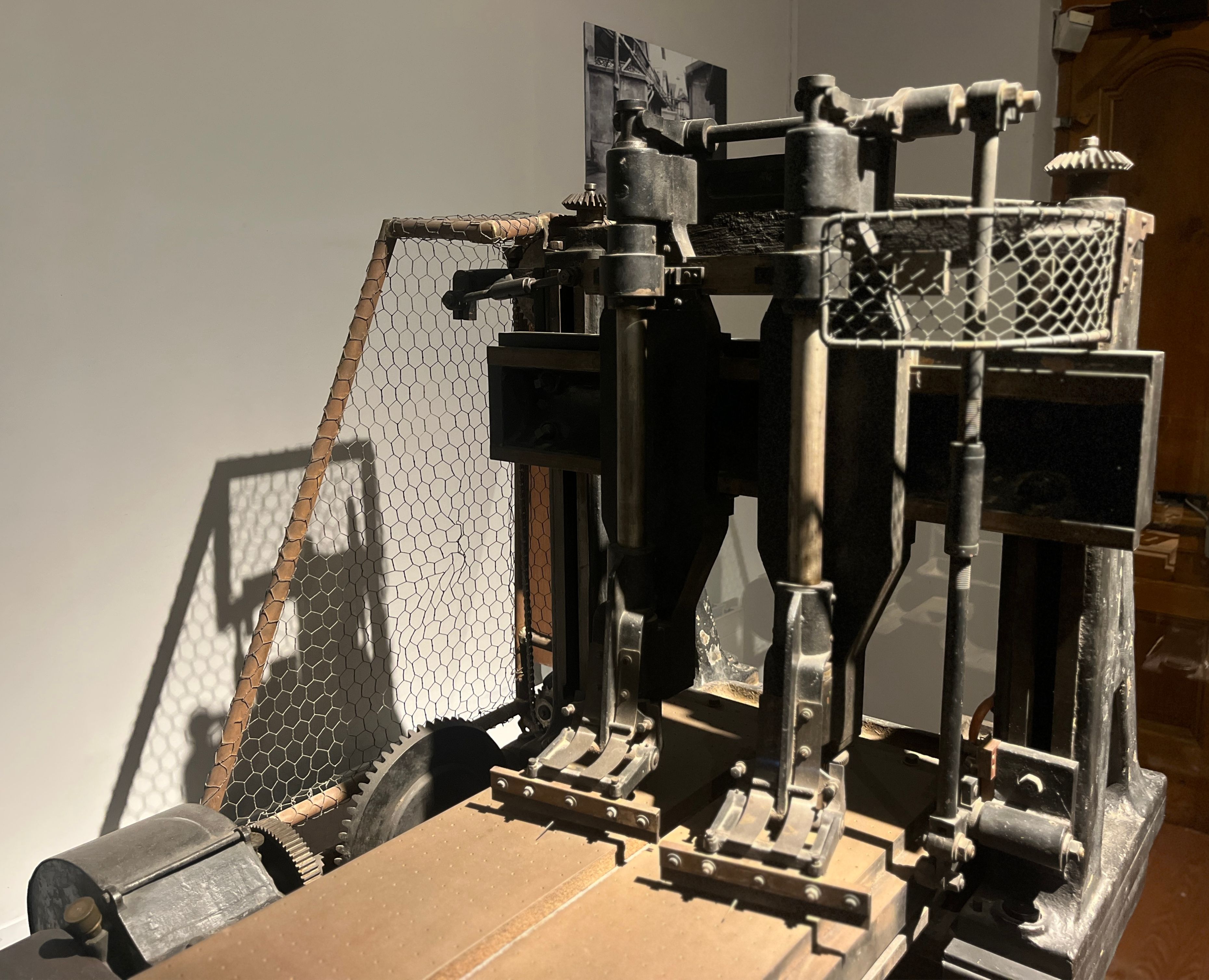 A metal rolling machine with gears, upright supports, a working bed and wire guards, displayed in a museum.
