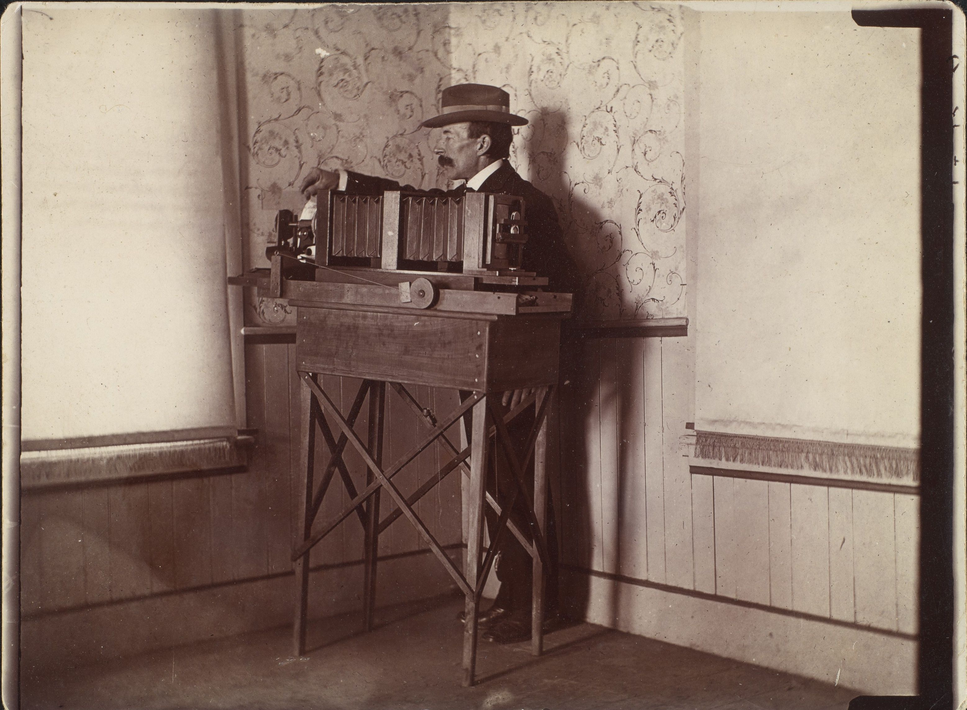 Wilson Bentley standing behind a long bellows camera mounted on a wooden table beside a window.