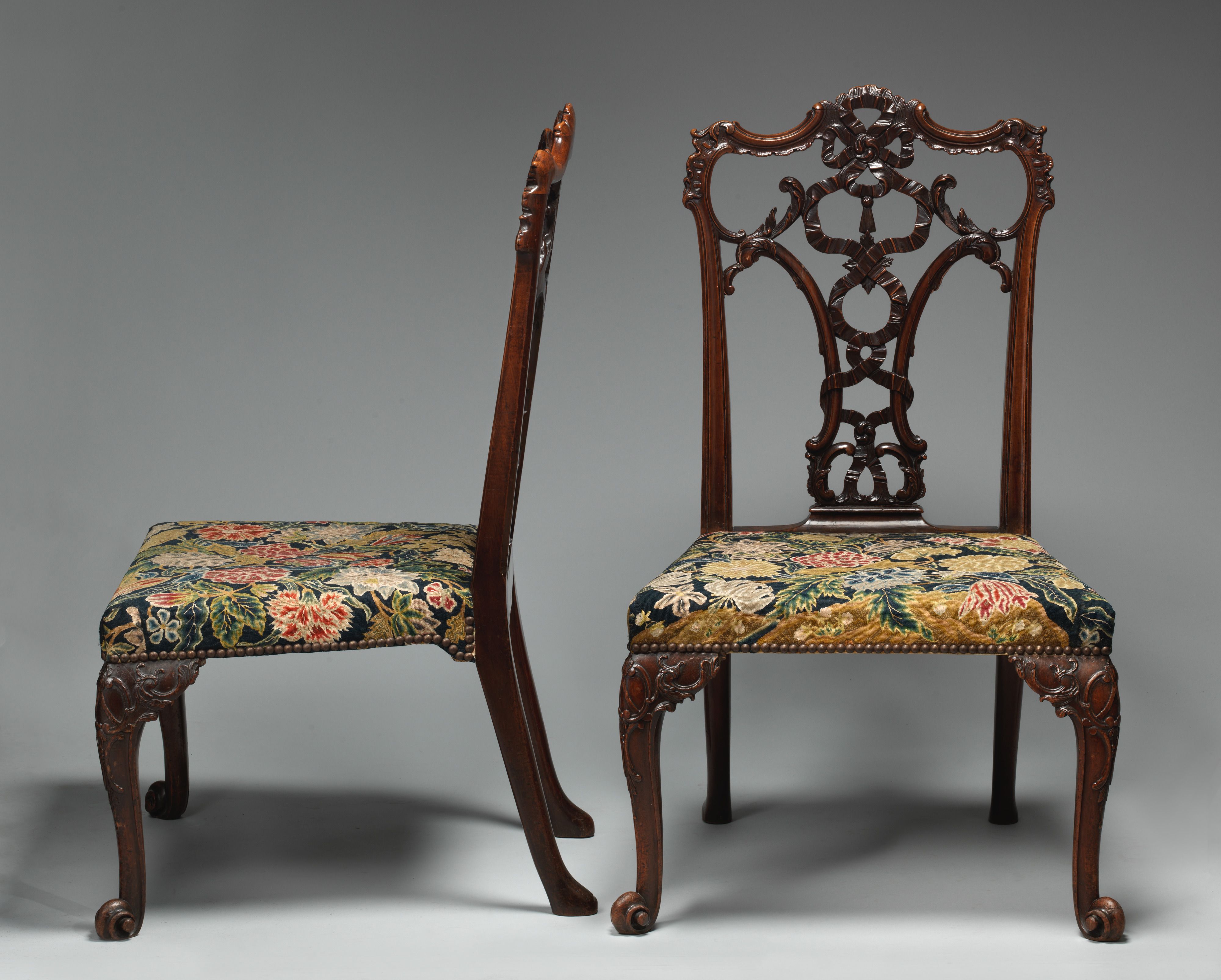 Two mahogany chairs, one seen from the side and the other from the front, with carved ribbon backs and flowered embroidered seats