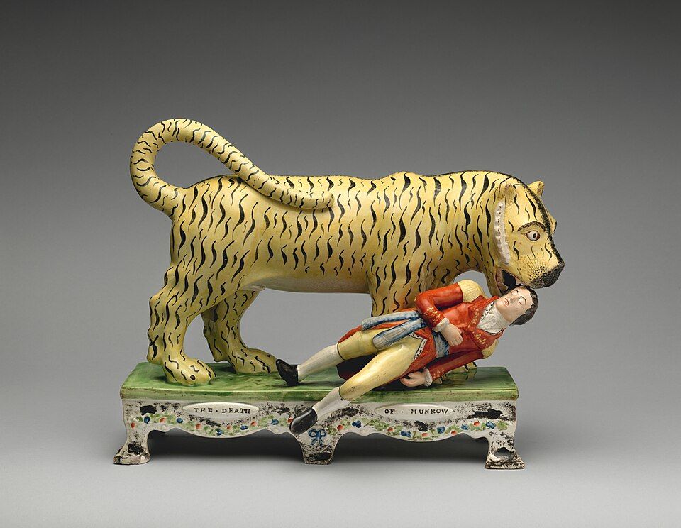 A yellow ceramic tiger standing over a red-coated man on a green and floral base.