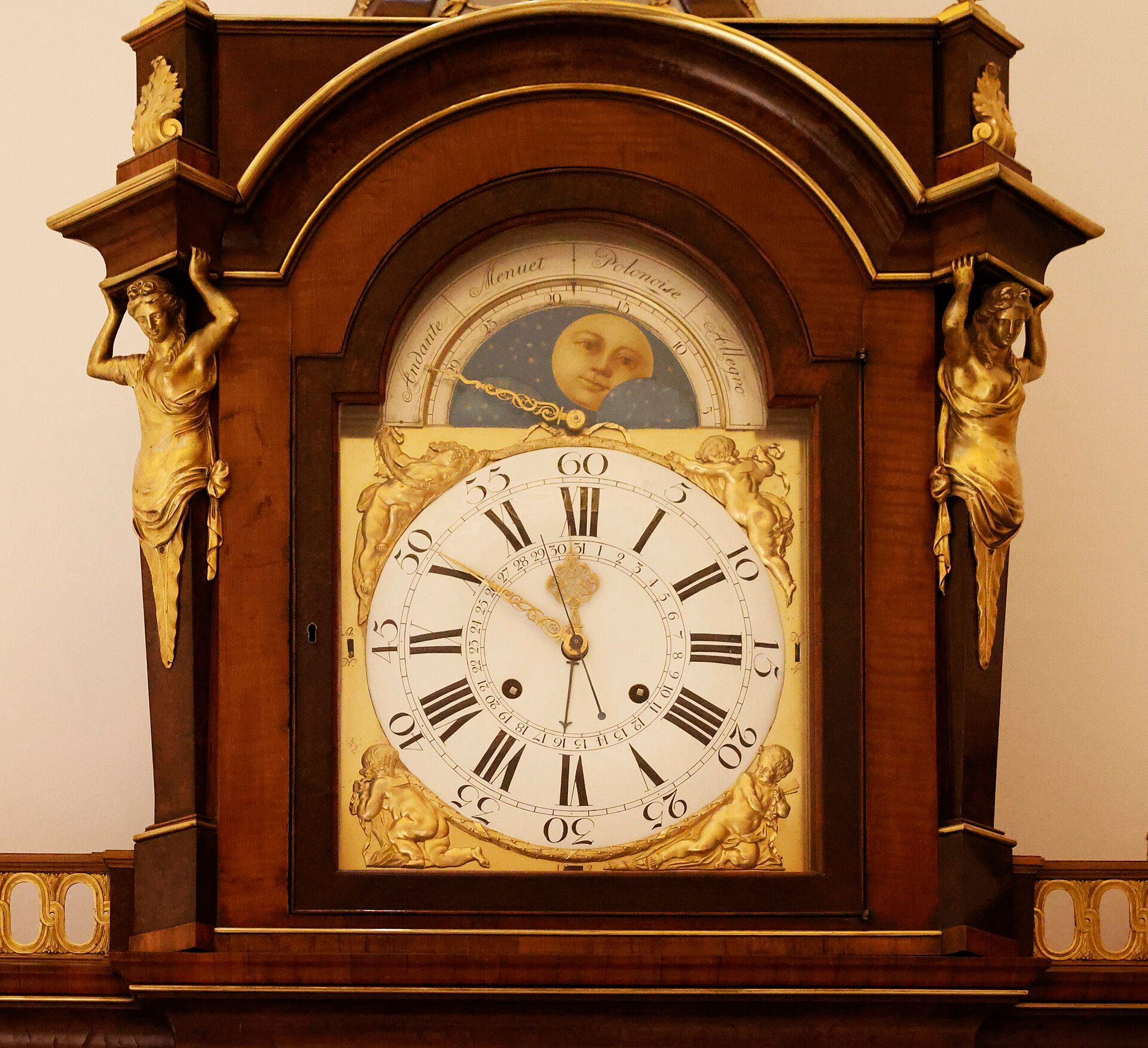 A white clock dial in a curved wooden superstructure with gilded ornamental mounts.