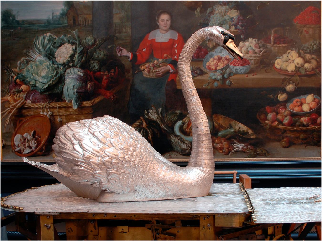 A life-size silver swan with a long curved neck standing on a bed of clear glass rods.