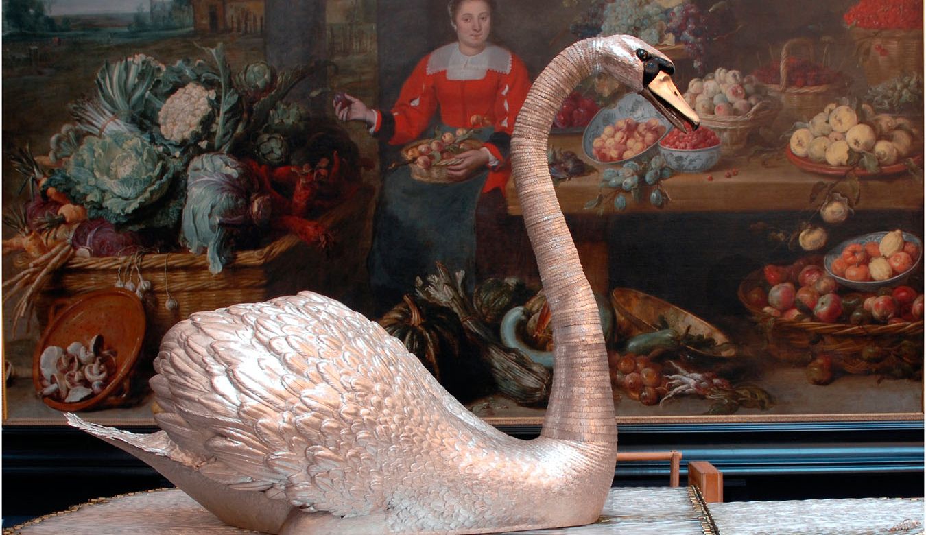 A life-size silver swan with a long curved neck standing on a bed of clear glass rods.