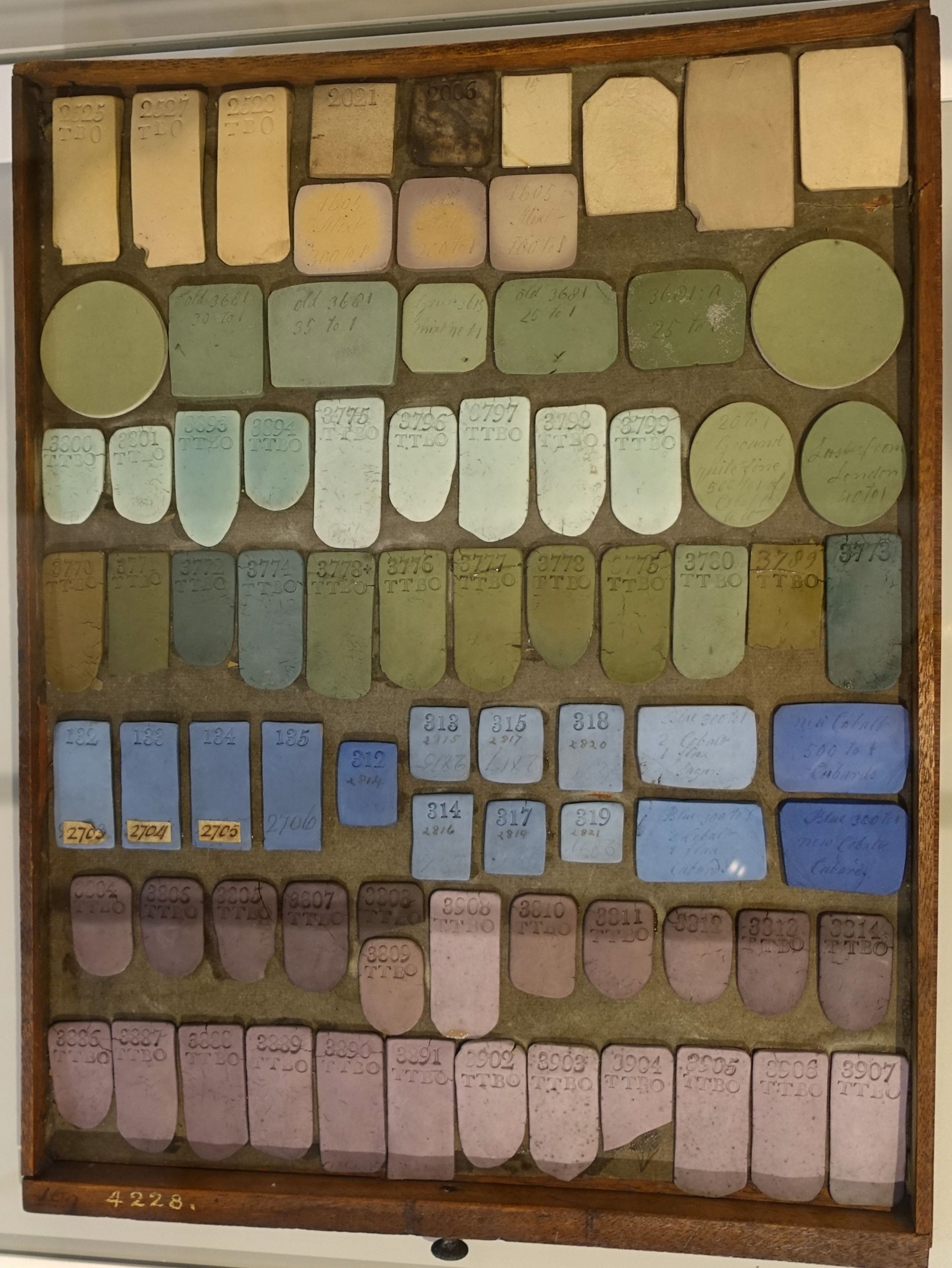 Numbered cream, green, blue and pink jasper material trials arranged in a wooden display frame