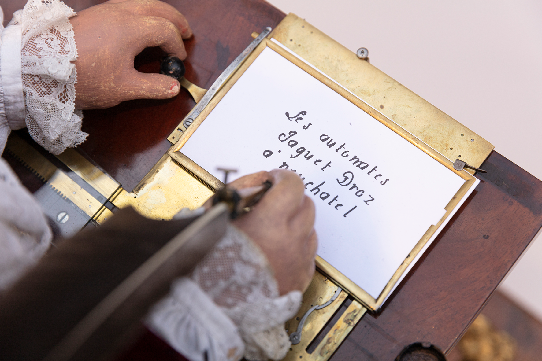 The Writer’s quill above a sheet bearing several lines naming the Jaquet-Droz automata and Neuchâtel.