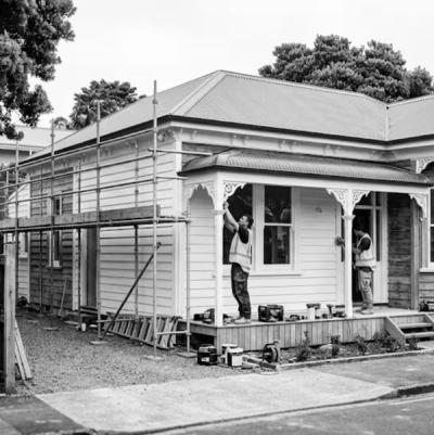 Painters on scaffolding restoring a weatherboard villa with decorative trim