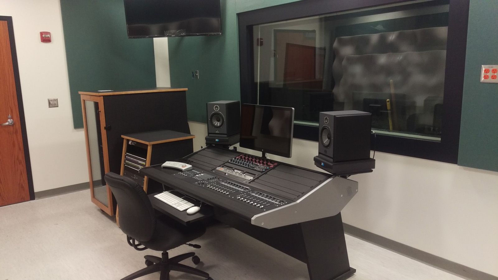 Control room with production desk, booth monitor, and equipment racks