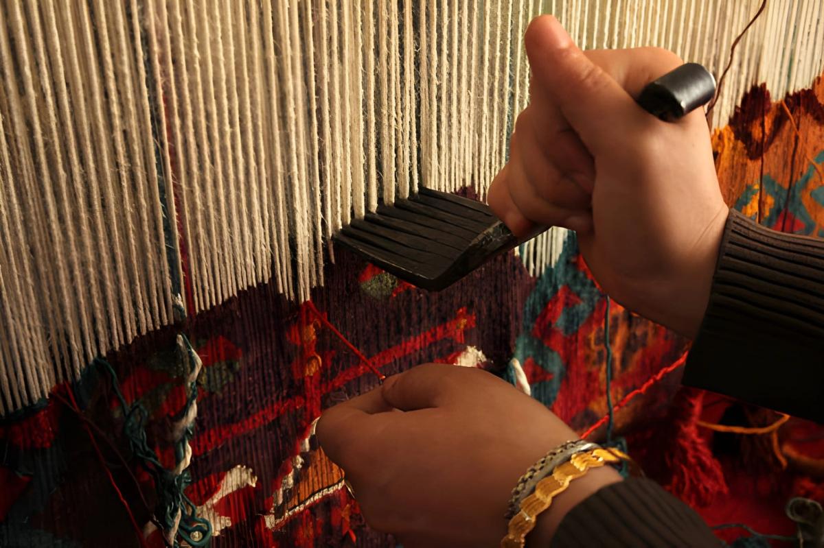 Artisan hands weaving rug threads on a traditional loom