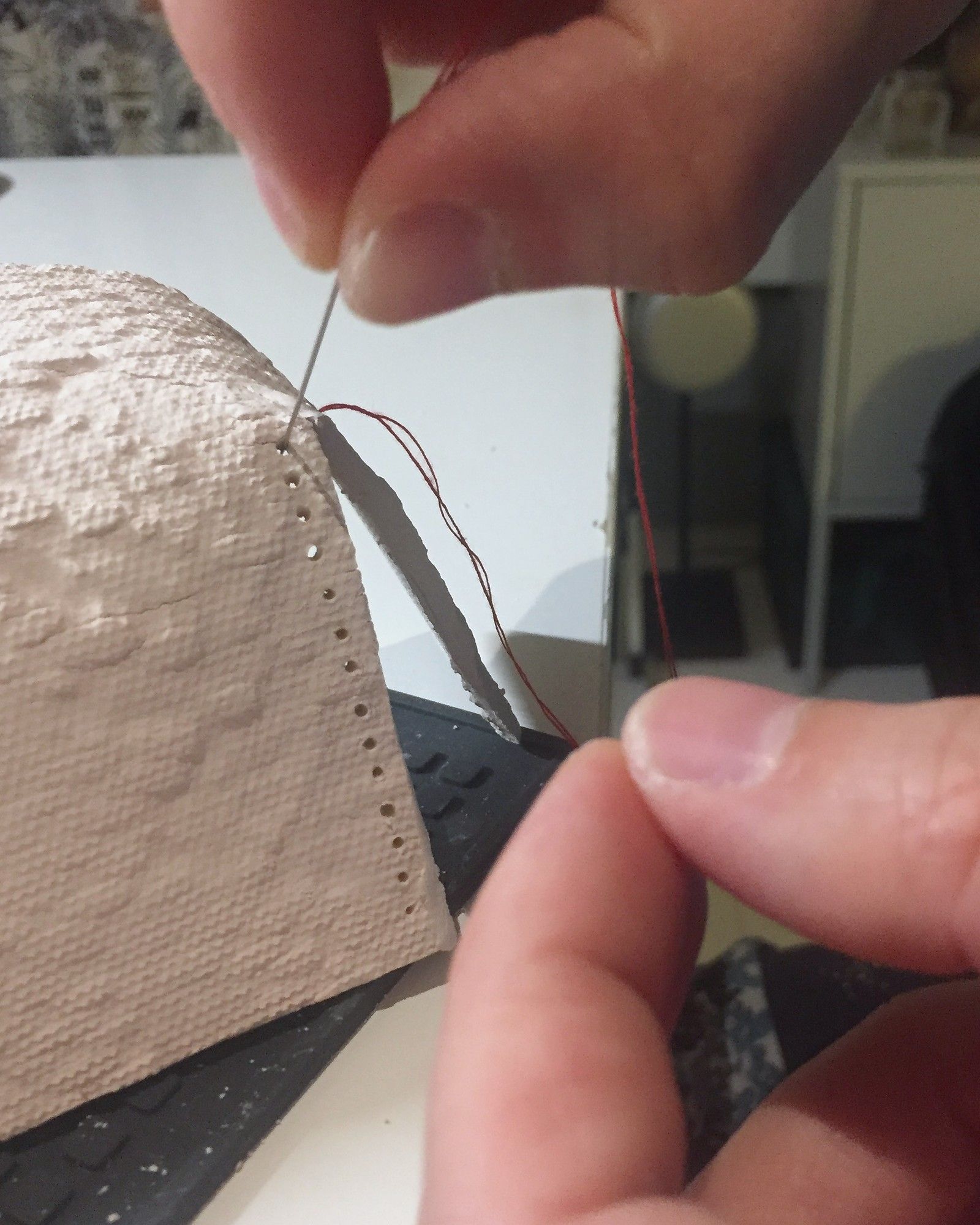 Two hands using a needle to stitch red thread through small holes along the edge of the clay F.