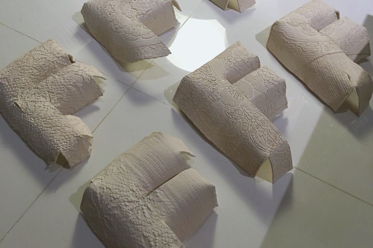 Several porcelain letters imprinted with different lace patterns, laid out on a pale tiled floor.