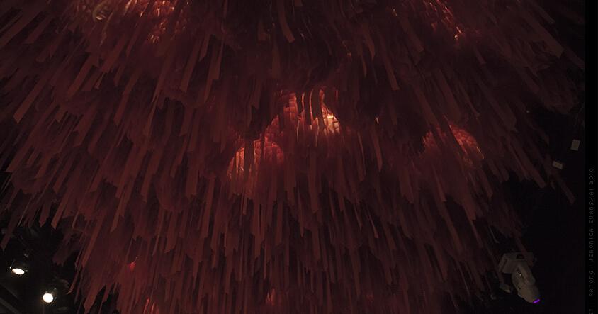 A ceiling densely covered with hanging reddish-brown ribbons, glowing with warm light.