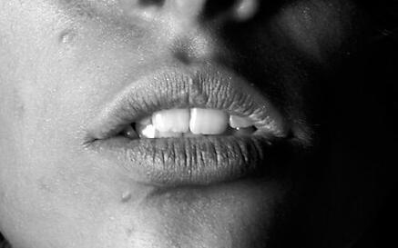 Black and white close-up of a person's face with a closed eye, parted lips, and one side in deep shadow.
