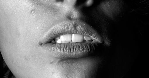 Black and white close-up of a person's face with a closed eye, parted lips, and one side in deep shadow.