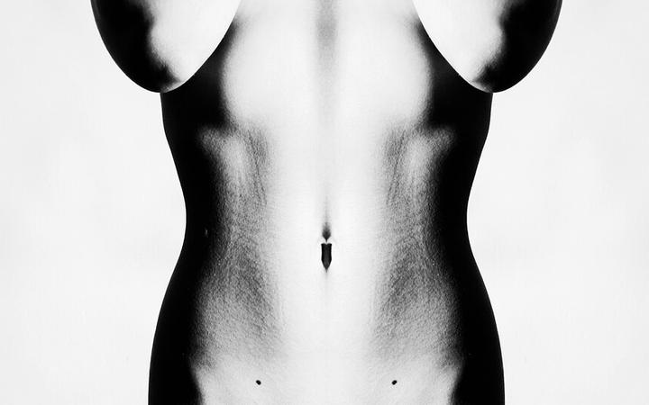 Symmetrical black and white photo of a bare human torso, featuring a navel and subtle body hair.