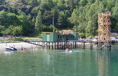 Badehus ved sandstrand og med bandande menneske omgitt av fin natur