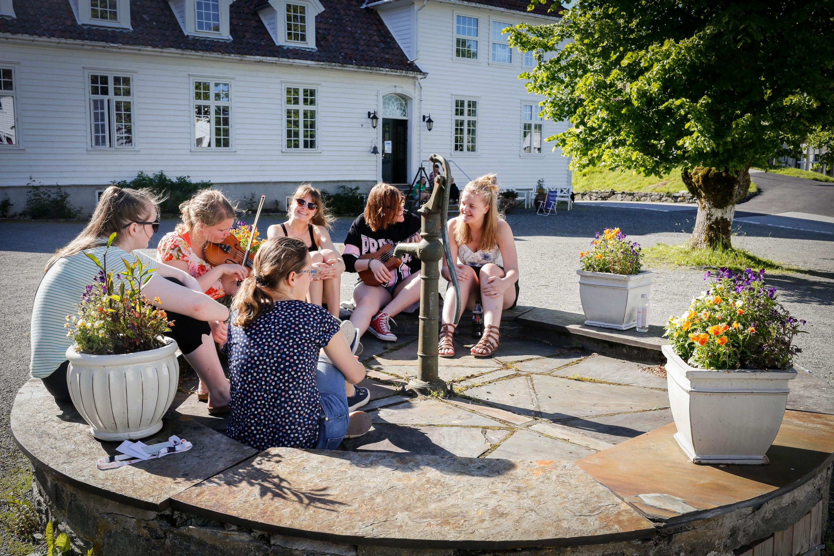 En gjeng med ungdommer sitter samlet og spiller fiolin og ukulele