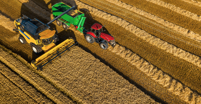 High-angle aerial view of a yellow combine harvester and a red tractor working together to harvest a grain field