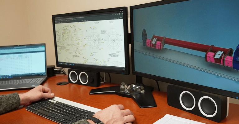 Engineer using dual desktop monitors and laptop to view 3D CAD modeling
