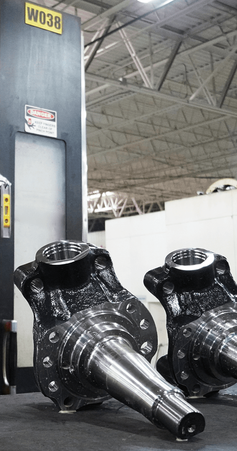A machine operator stands at a CNC machine with two parts on a table
