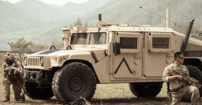 Military tactical vehicle parked on a dry field with soldiers in gear nearby