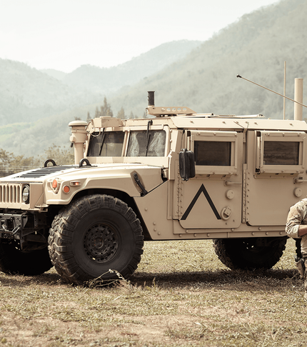 Military tactical vehicle parked on a dry field with soldiers in gear nearby