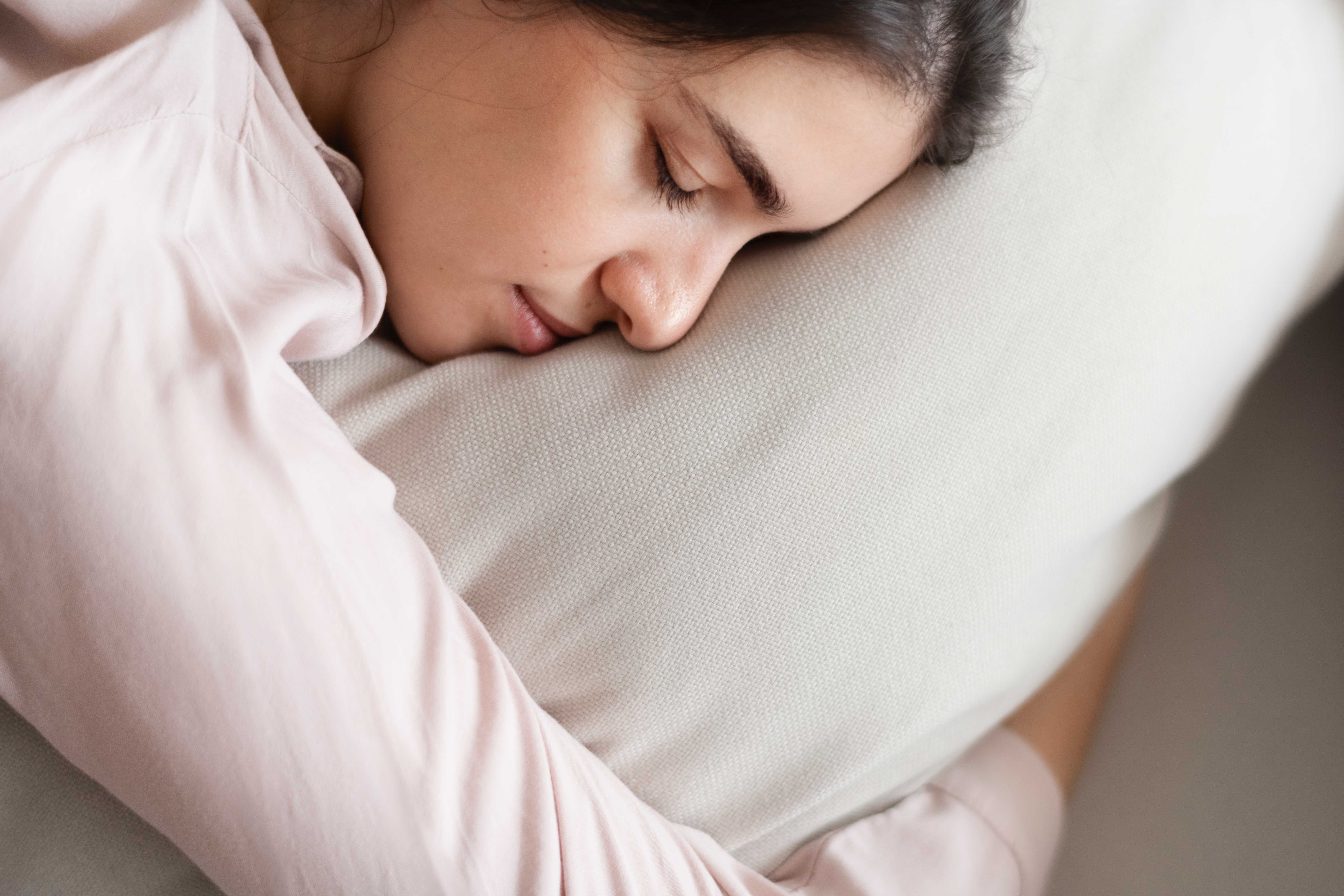 Femme endormie paisiblement, allongée sur un coussin clair, illustrant un sommeil profond et réparateur dans un environnement calme et apaisant