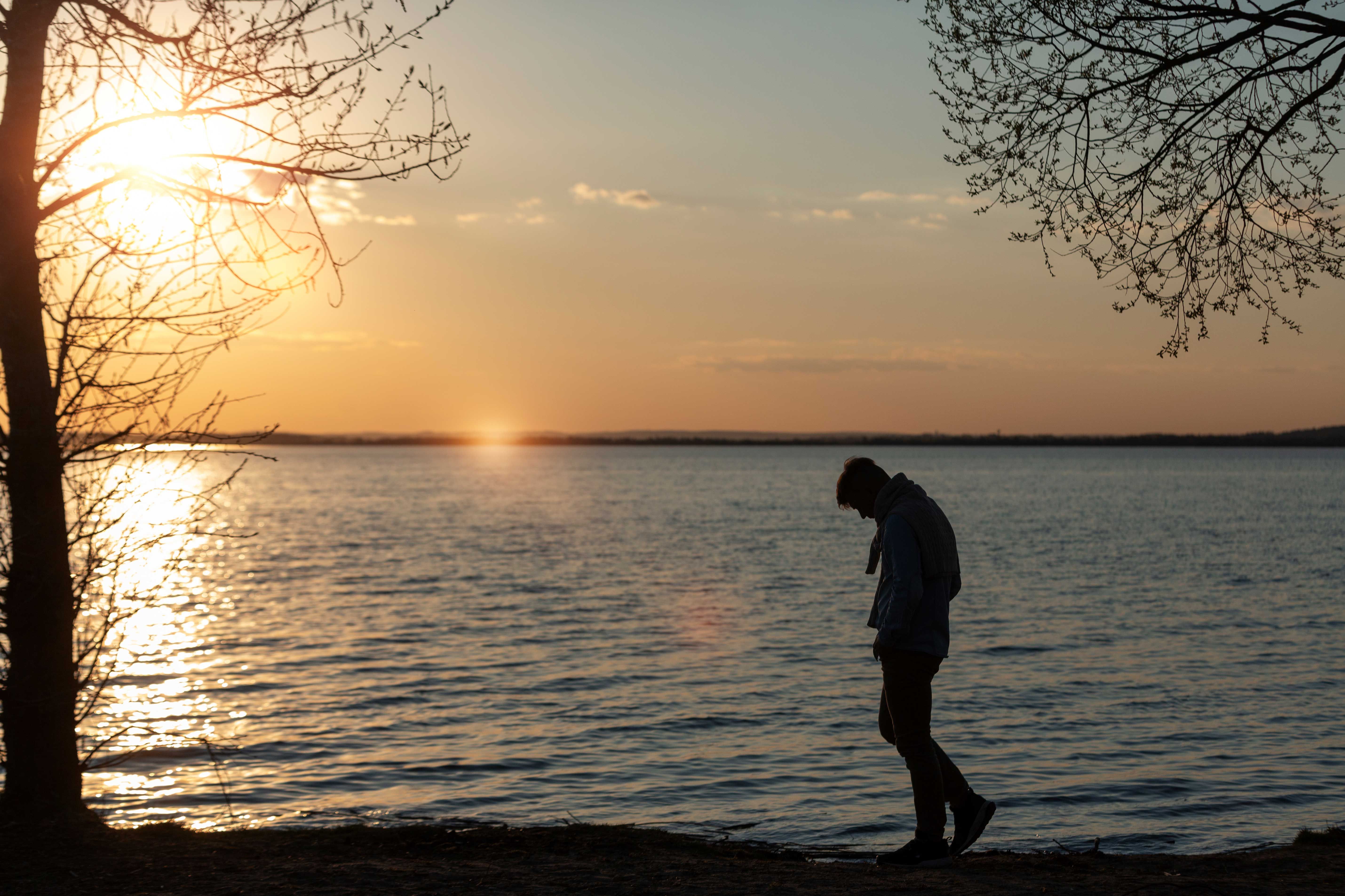 Personne seule marchant au bord de l’eau au coucher du soleil, en pleine introspection liée au deuil.