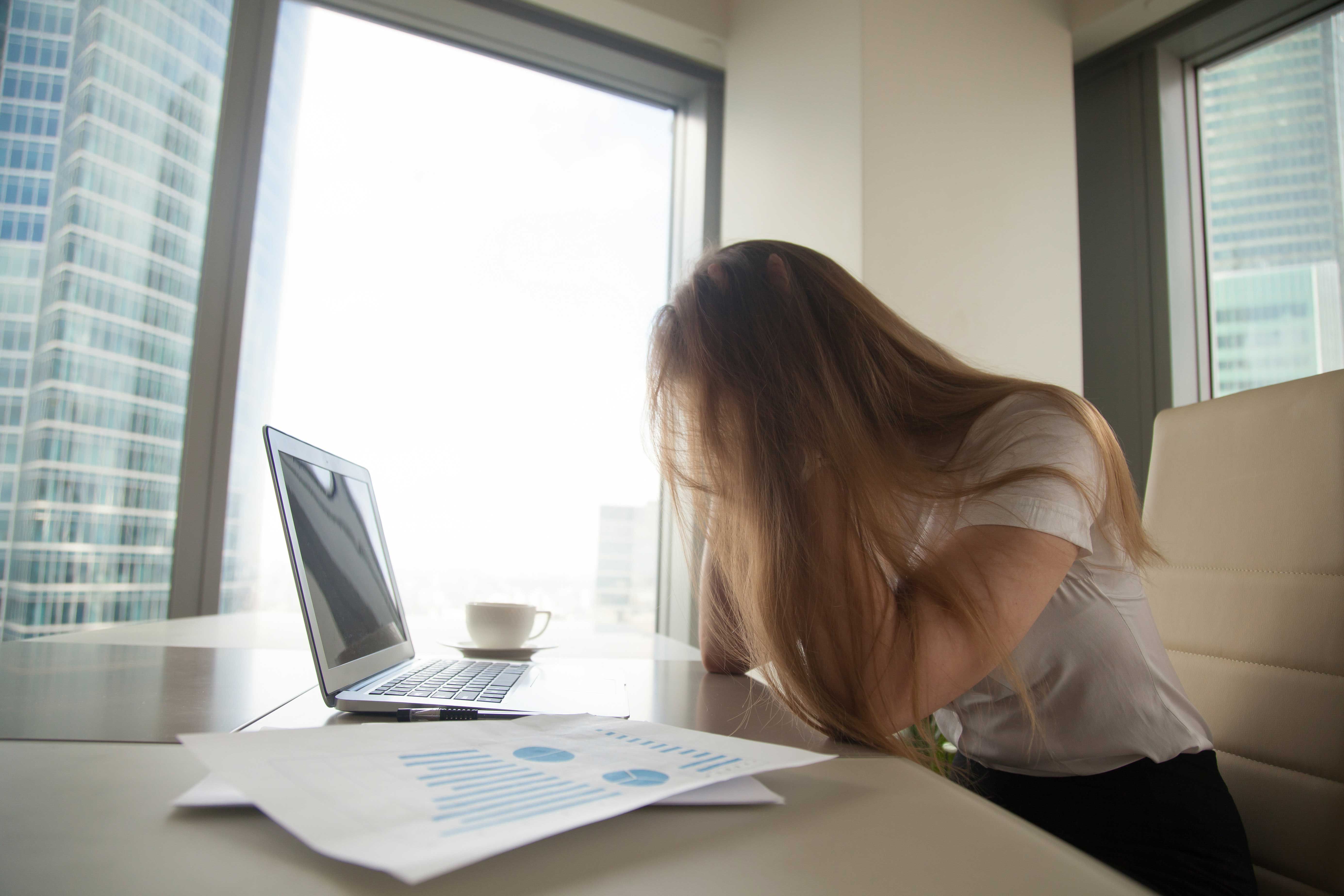 Femme assise à un bureau, tête baissée devant un ordinateur, exprimant fatigue et épuisement liés au burn-out.