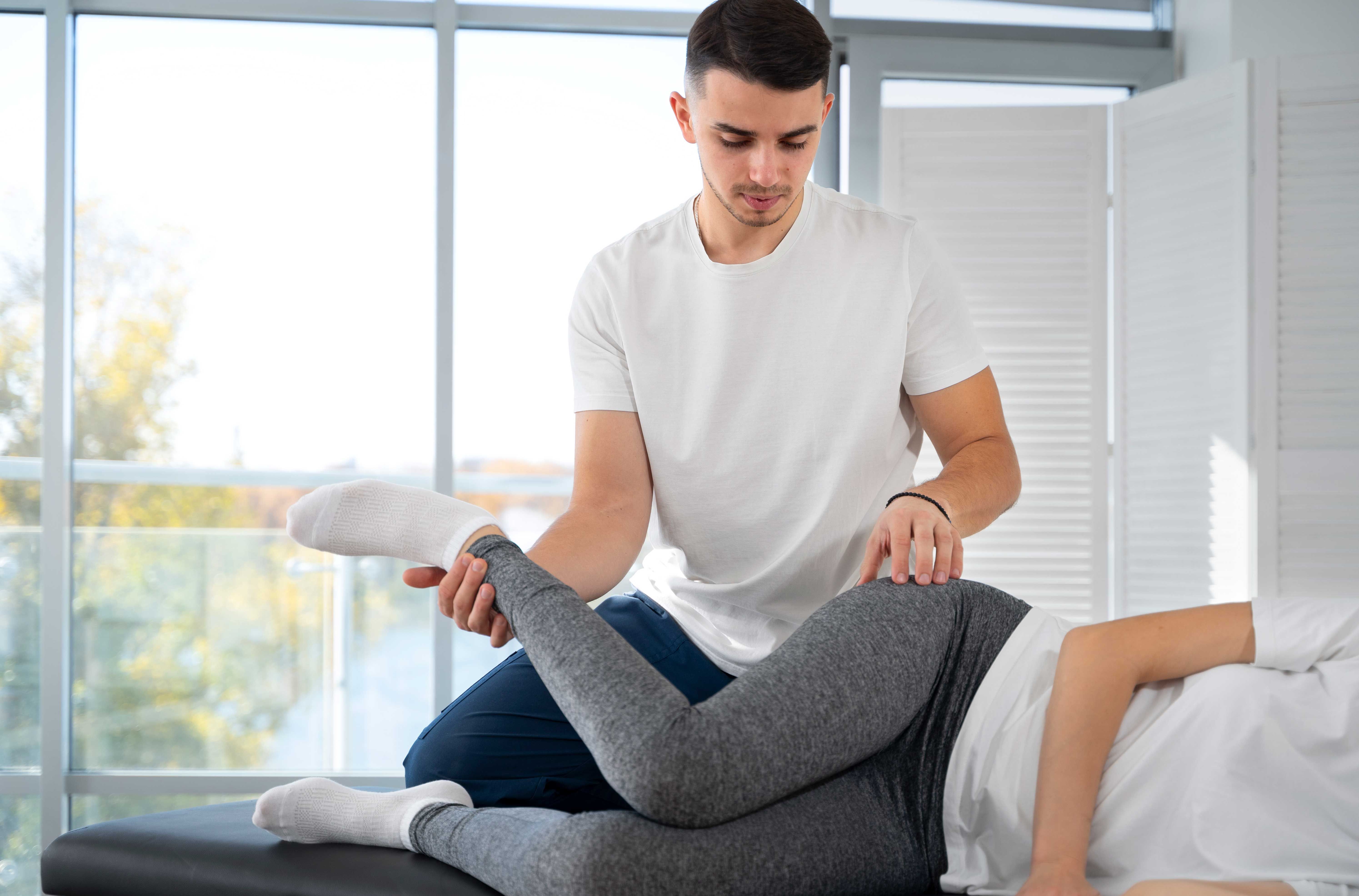Ostéopathe mobilisant la jambe d’un patient allongé pour évaluer une pathologie musculaire ou articulaire, dans un cabinet lumineux.