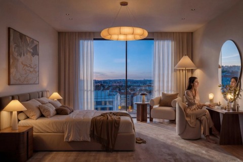 Woman sitting at a dressing table in a bedroom lit at dusk, with a city view.