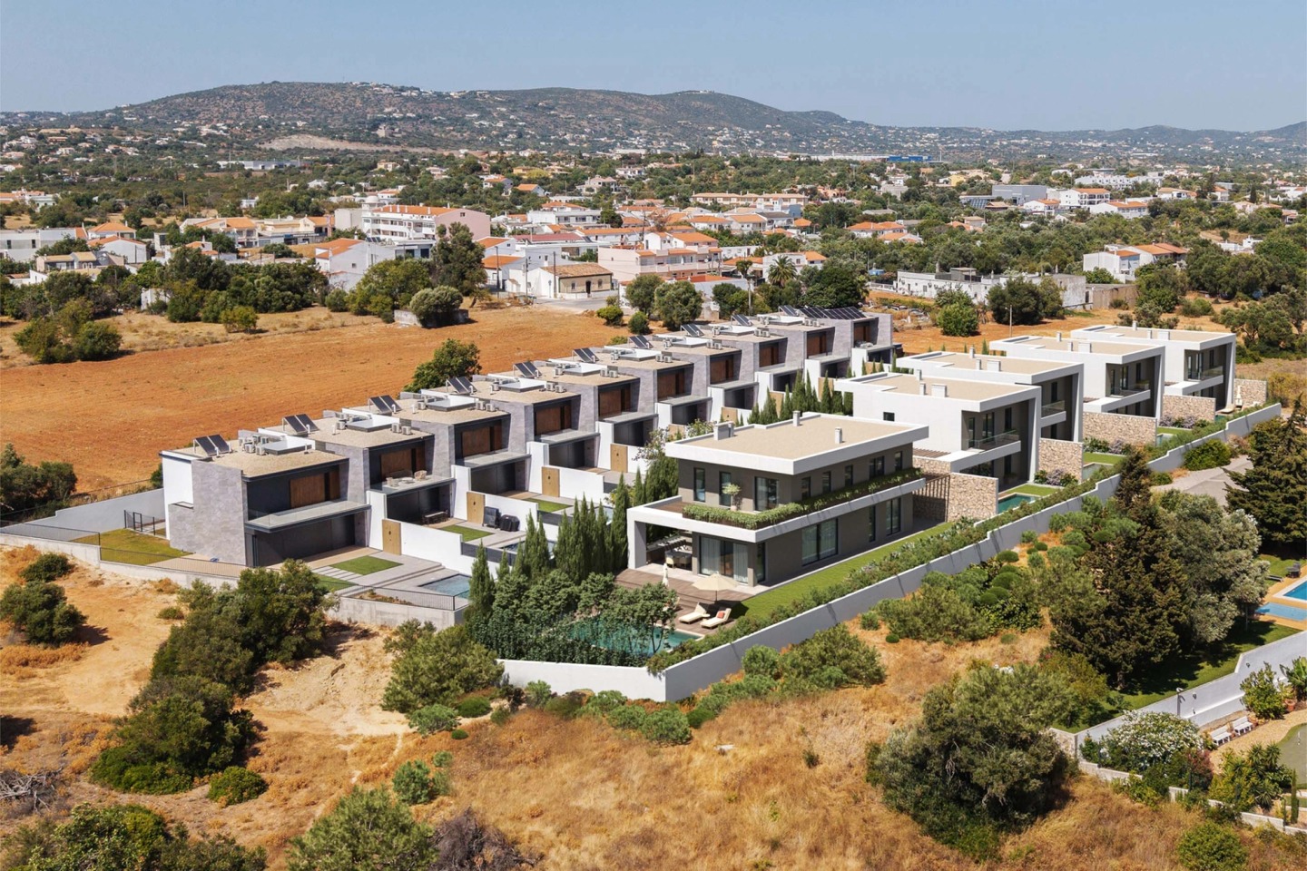 Aerial view of Pearl Villas in Almancil, a row of villas with pools among the scrub and the hills beyond.