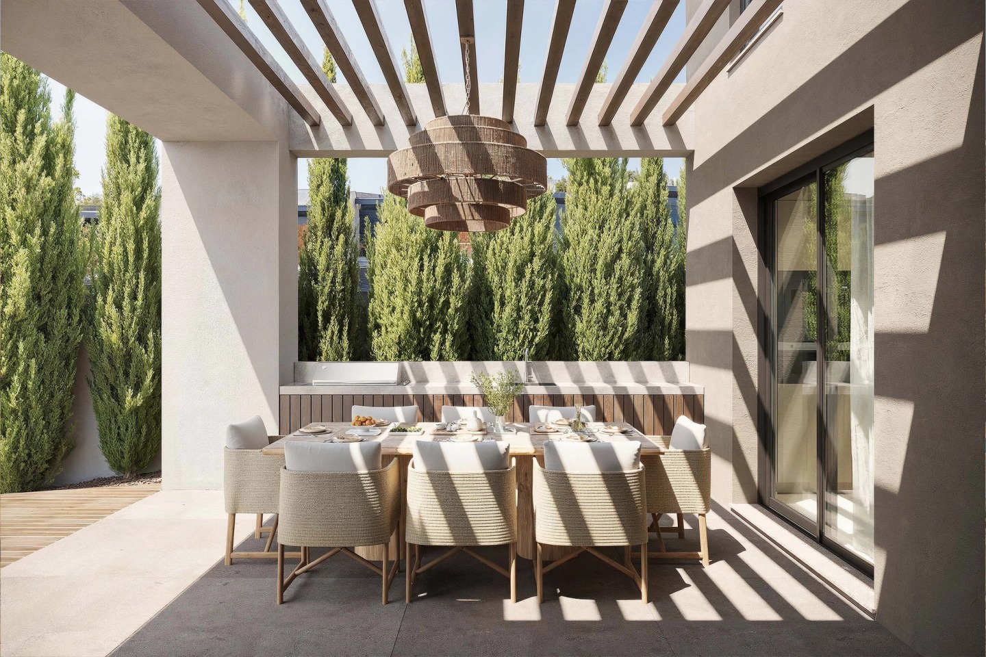 Outdoor dining table under a pergola casting striped shadows, with cypresses behind.